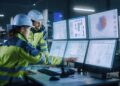 Industry 4.0 Modern Factory: Project Engineer Talks to Female Operator who Controls Facility Production Line, Uses Computer with Screens Showing AI, Machine Learning Enhanced Assembly Process