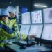 Industry 4.0 Modern Factory: Project Engineer Talks to Female Operator who Controls Facility Production Line, Uses Computer with Screens Showing AI, Machine Learning Enhanced Assembly Process